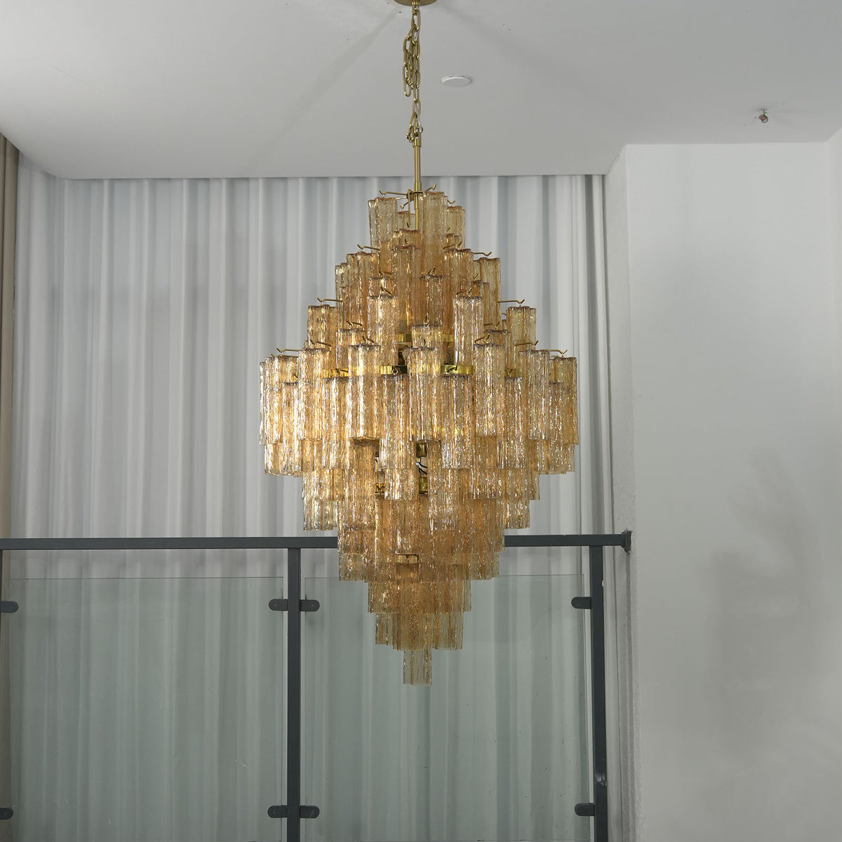 Addis Diamond Chandelier with glowing amber glass hanging in a room with sheer curtains