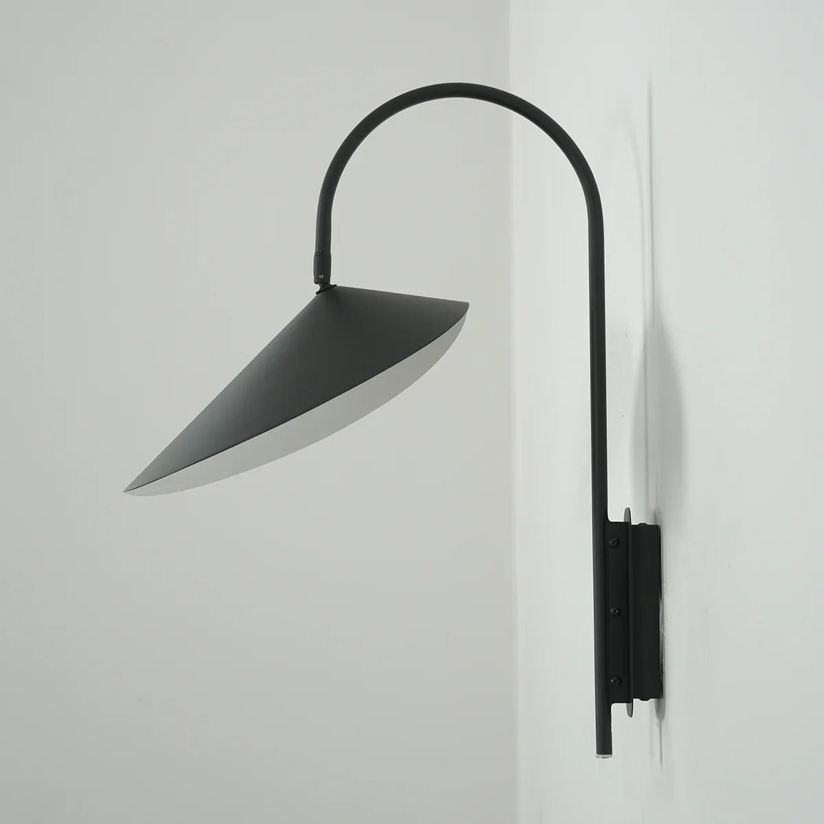 Front view of the lit Arum Swivel Wall Lamp in matte black on a plain white wall