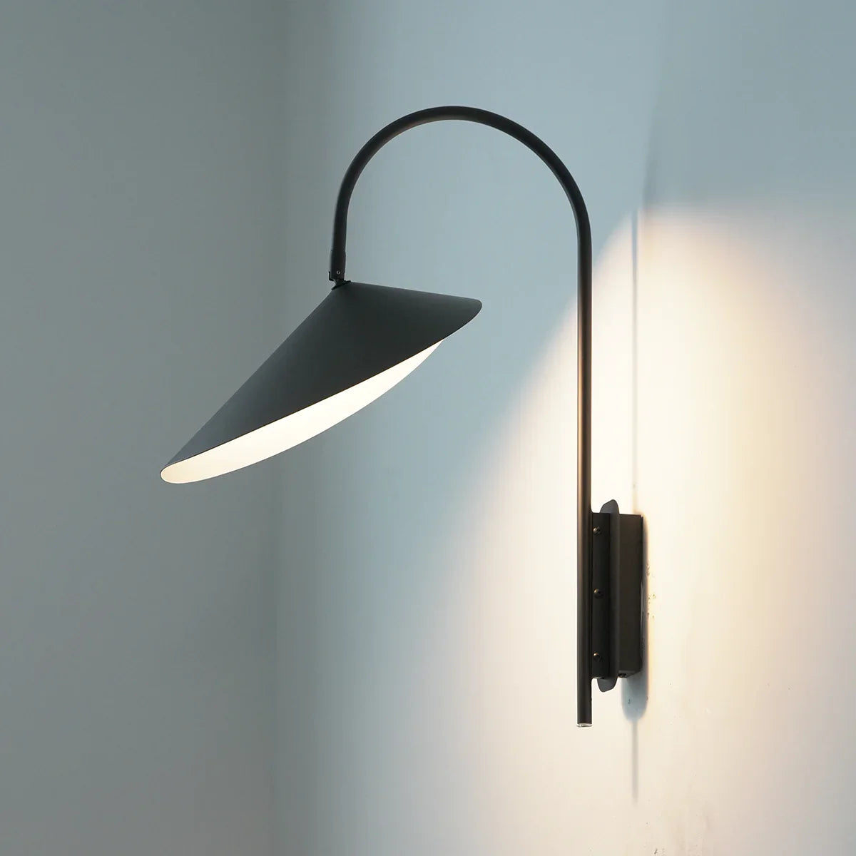 Side view of the lit Arum Swivel Wall Lamp in matte black on a plain white wall