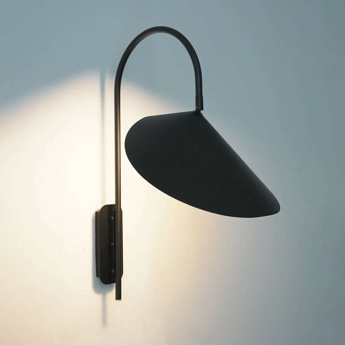 Top view of the lit Arum Swivel Wall Lamp in matte black on a plain white wall