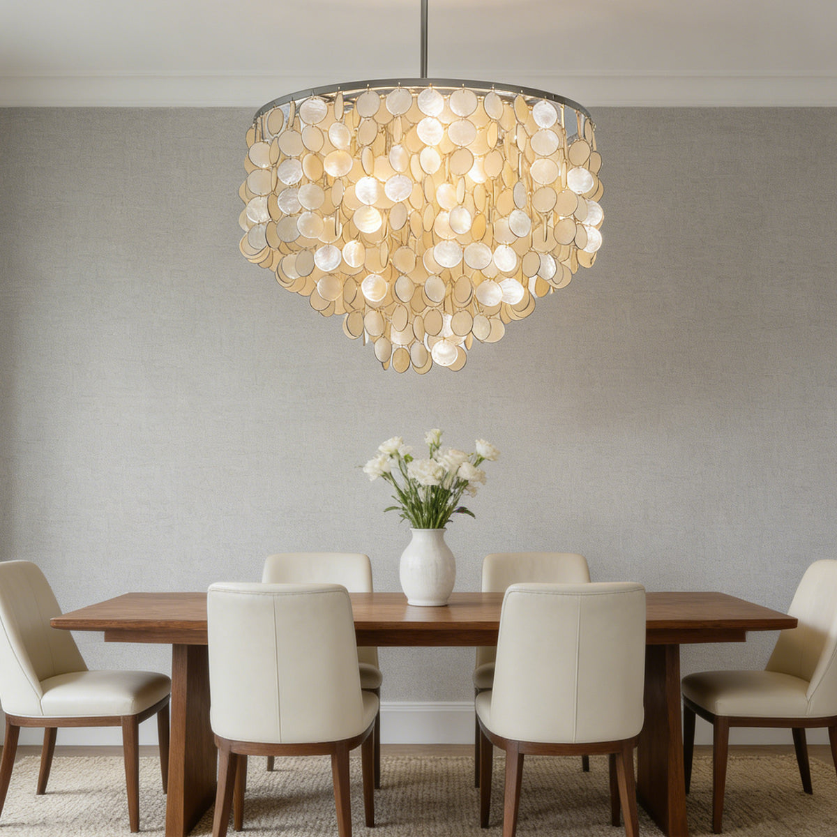 Capiz shell round chandelier centered above a wooden dining table with white upholstered chairs.