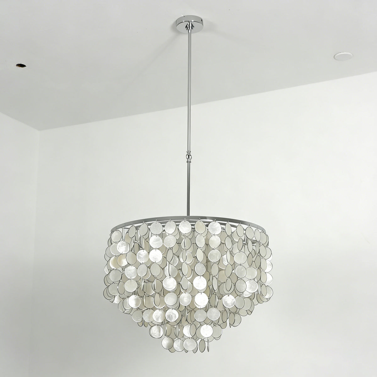 Low-angle view of a capiz shell round chandelier hanging from a ceiling in a minimalist room.