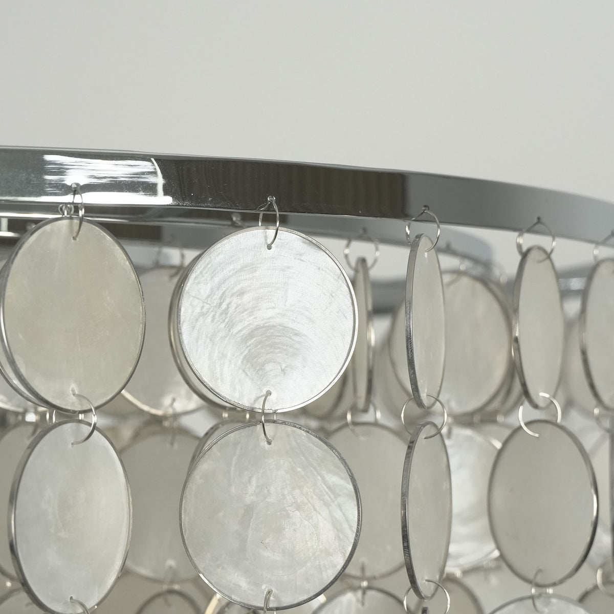 Close-up of the polished chrome frame and layered capiz shell discs on the round chandelier.