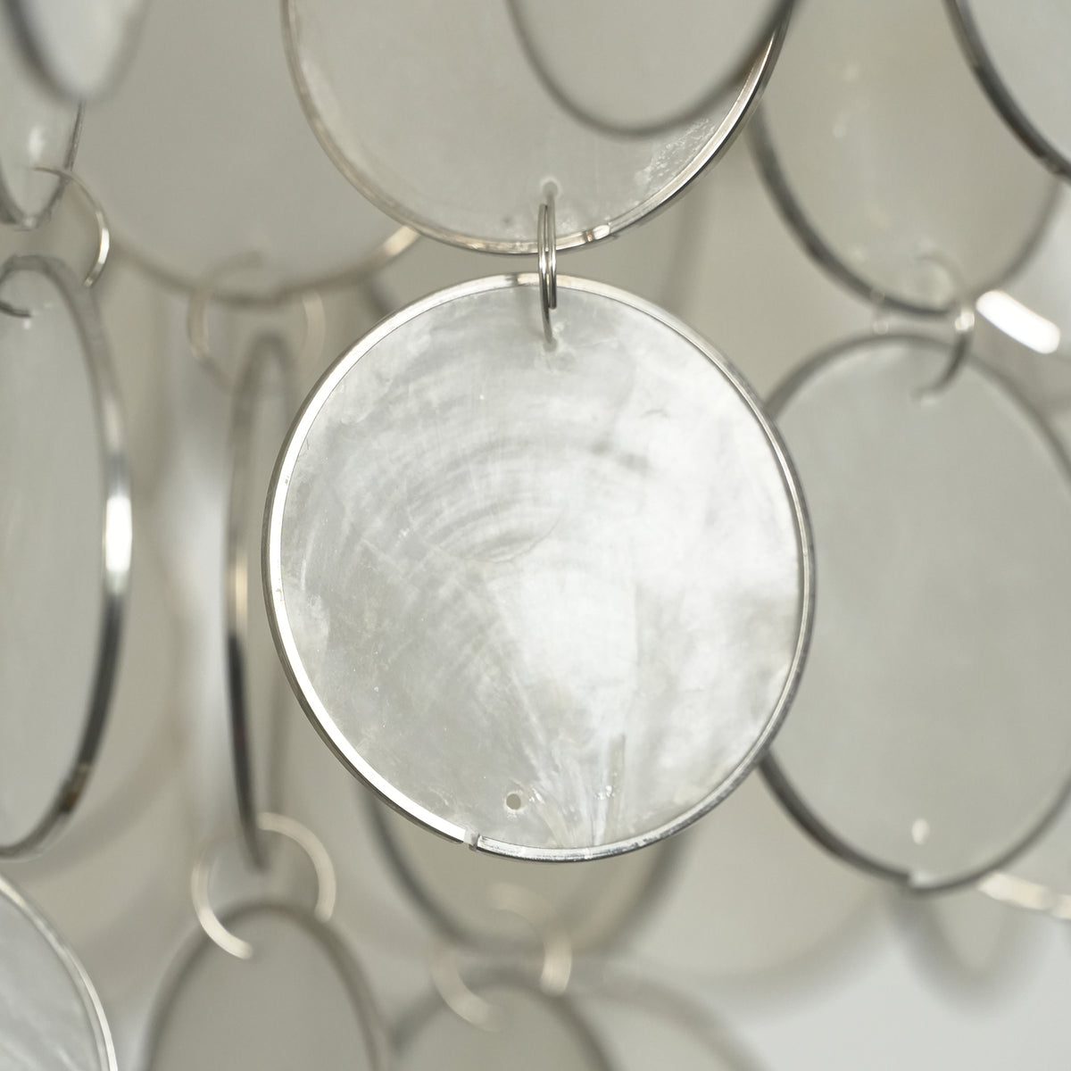 Close-up of a single iridescent capiz shell disc hanging on the round chandelier, showing its natural texture.