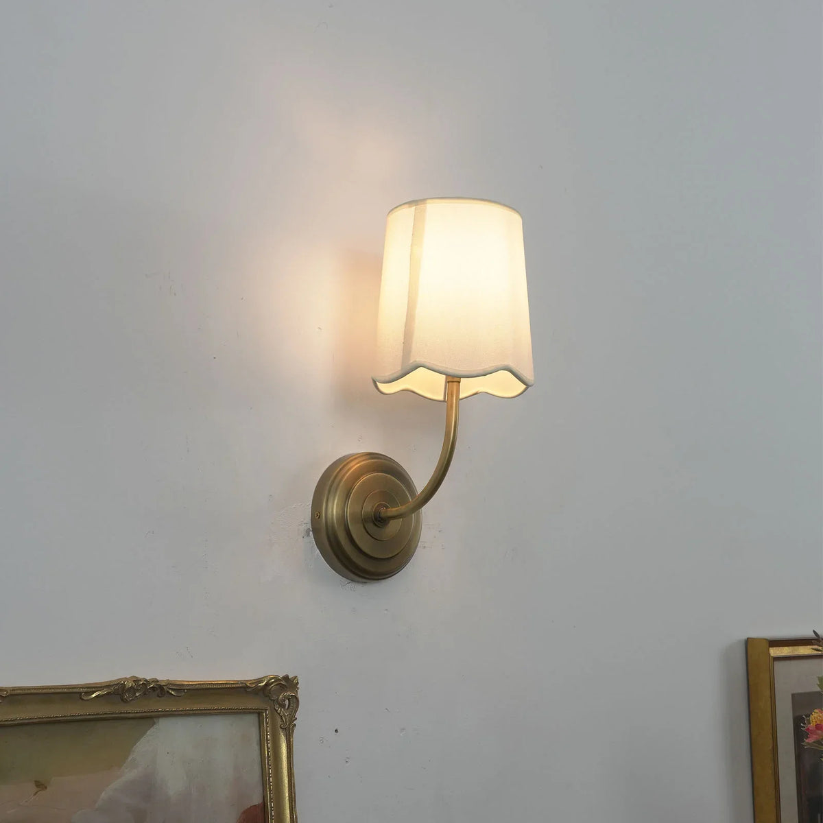 Lit Curved Arm Fabric Wall Sconce with soft light and framed art in background