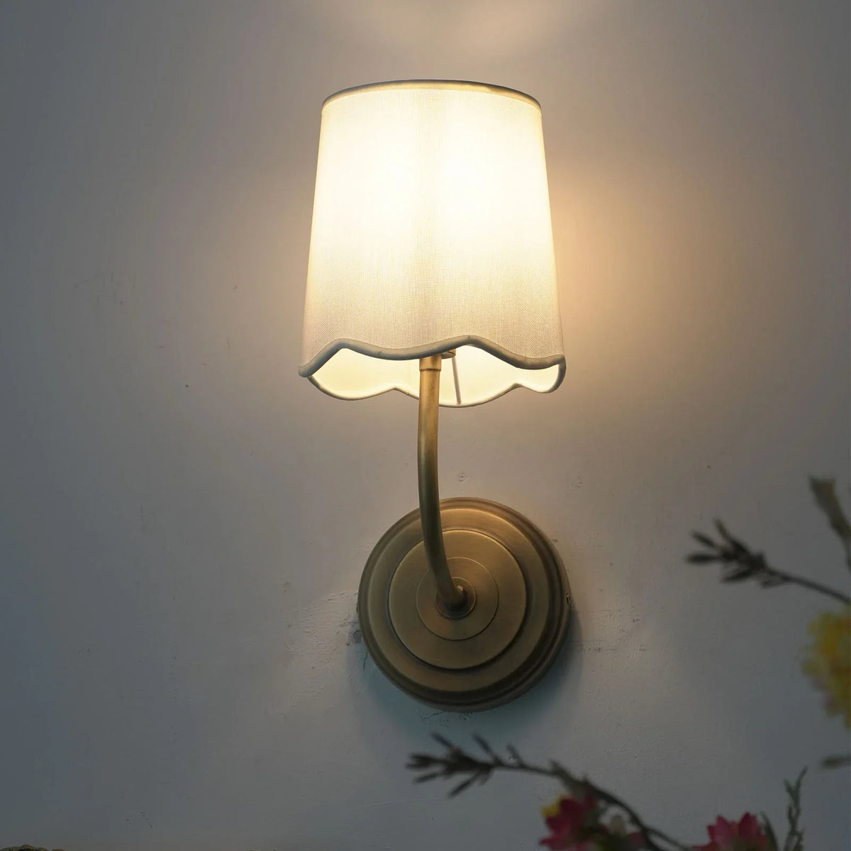 Lit Curved Arm Fabric Wall Sconce with warm light, corner view with floral decor