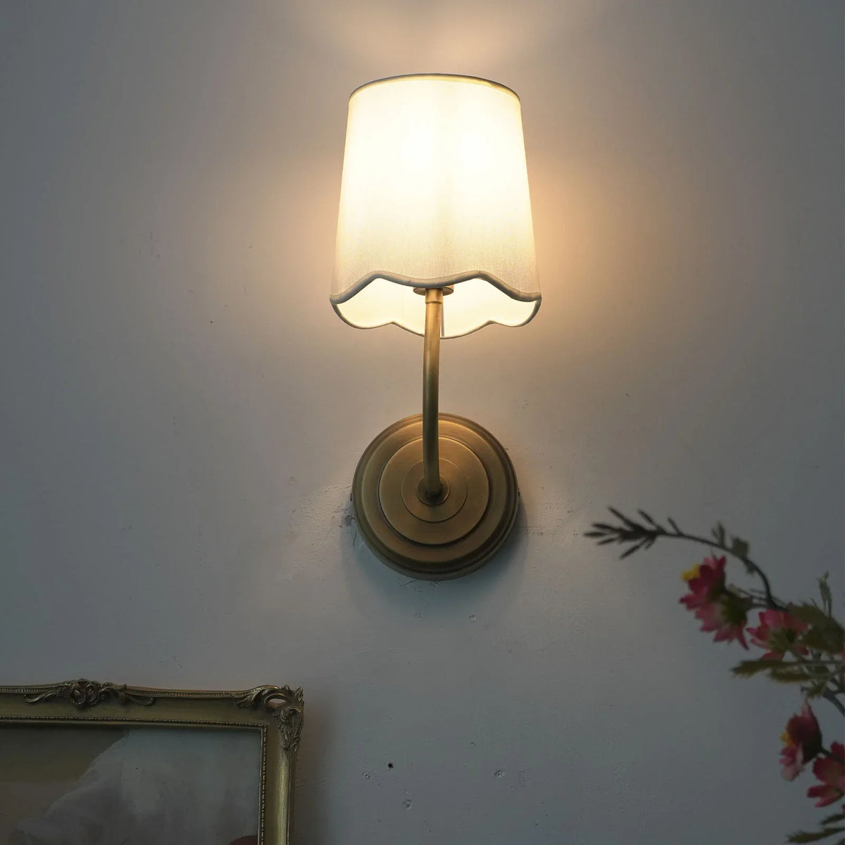 Lit Curved Arm Fabric Wall Sconce with soft light, front view with framed art
