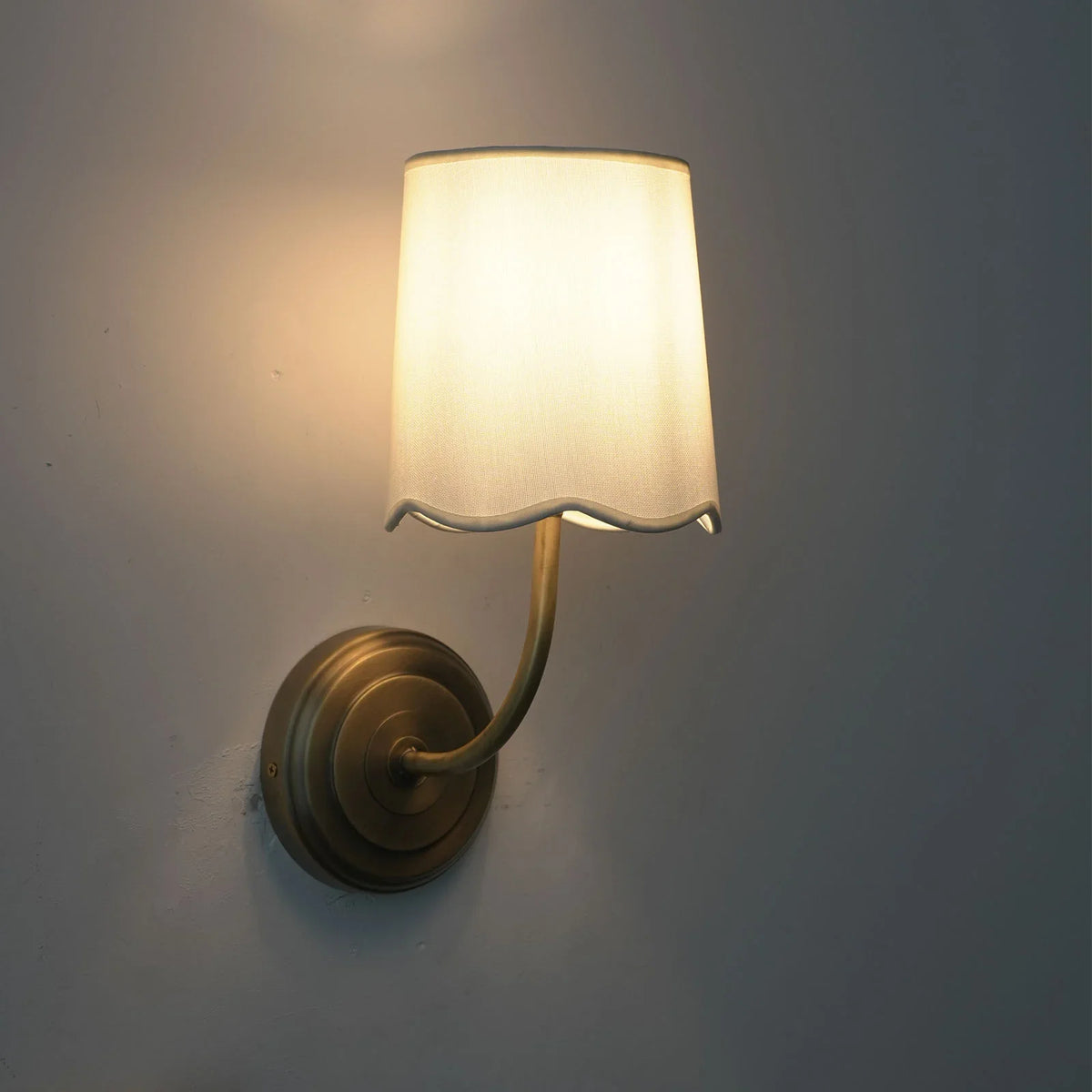 Lit Curved Arm Fabric Wall Sconce with warm light projection on a white wall