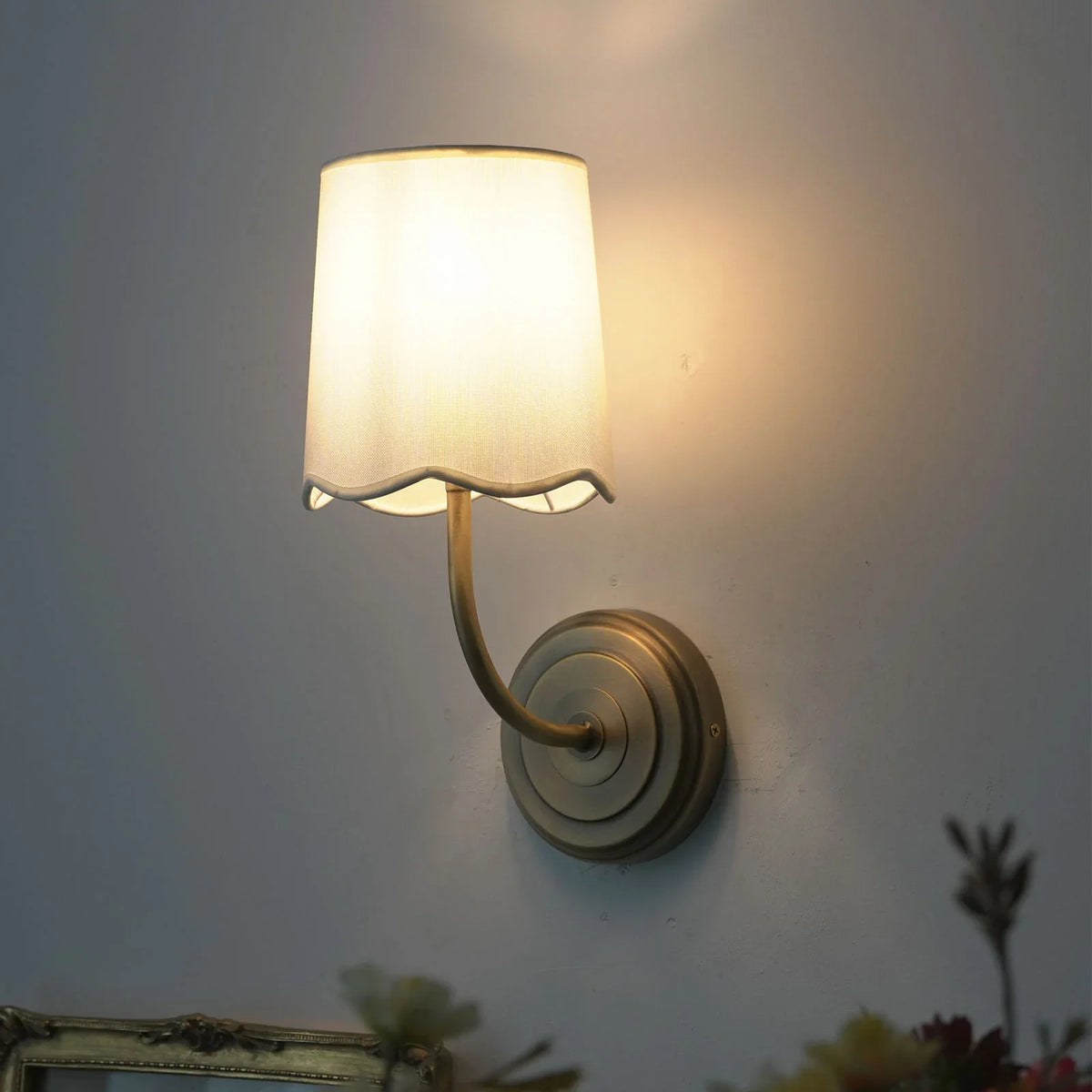 Lit Curved Arm Fabric Wall Sconce with soft glow, side view with floral accents