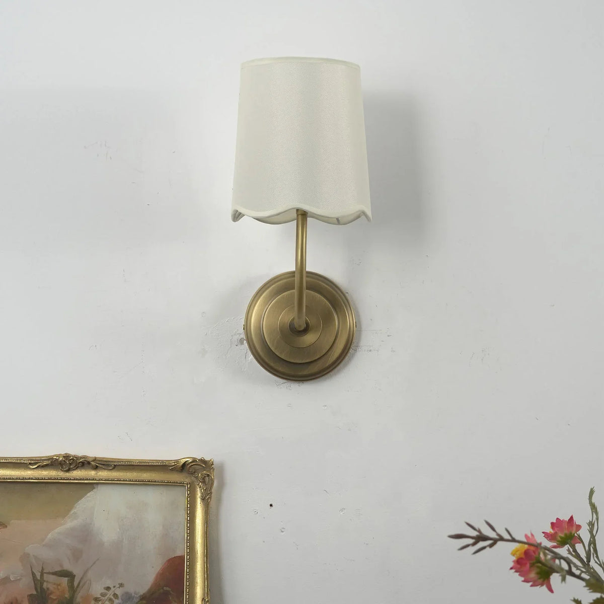 Unlit Curved Arm Fabric Wall Sconce with cream shade and floral decor in background
