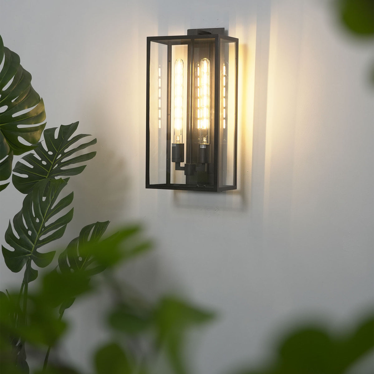 Faraday outdoor wall sconce mounted on a plain white wall, casting soft warm light.