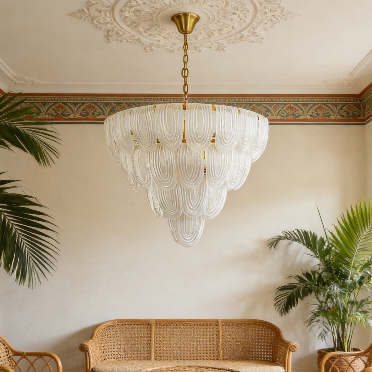Layered glass petal chandelier hanging in a bohemian-style living room with rattan furniture and tropical plants.