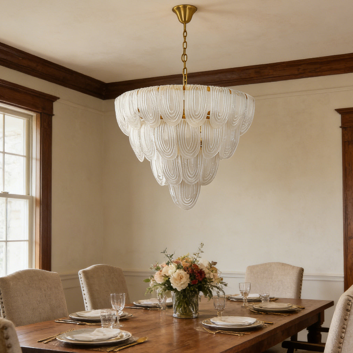 Layered glass petal chandelier hanging above a wooden dining table with white upholstered chairs.