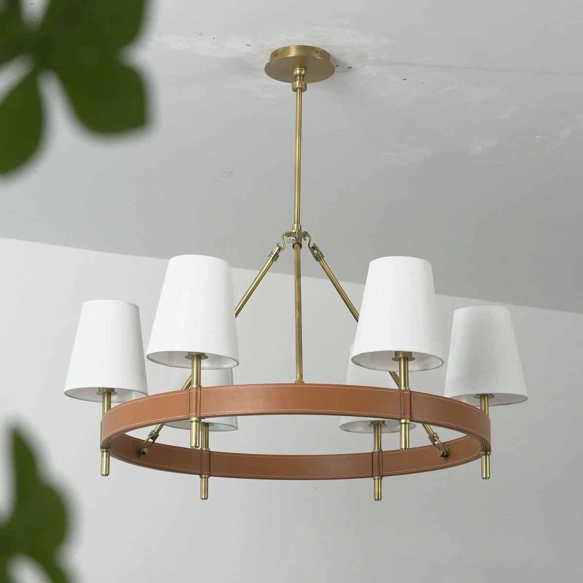 Front view of the round Leather Halo Ring Chandelier with greenery in background