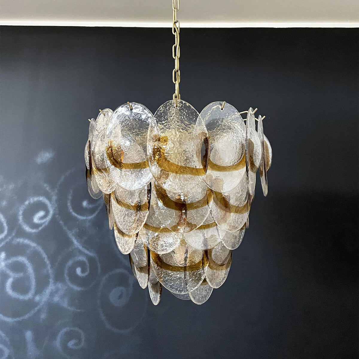 Mazzega-style amber glass chandelier hanging against a dark wall with subtle swirl patterns.