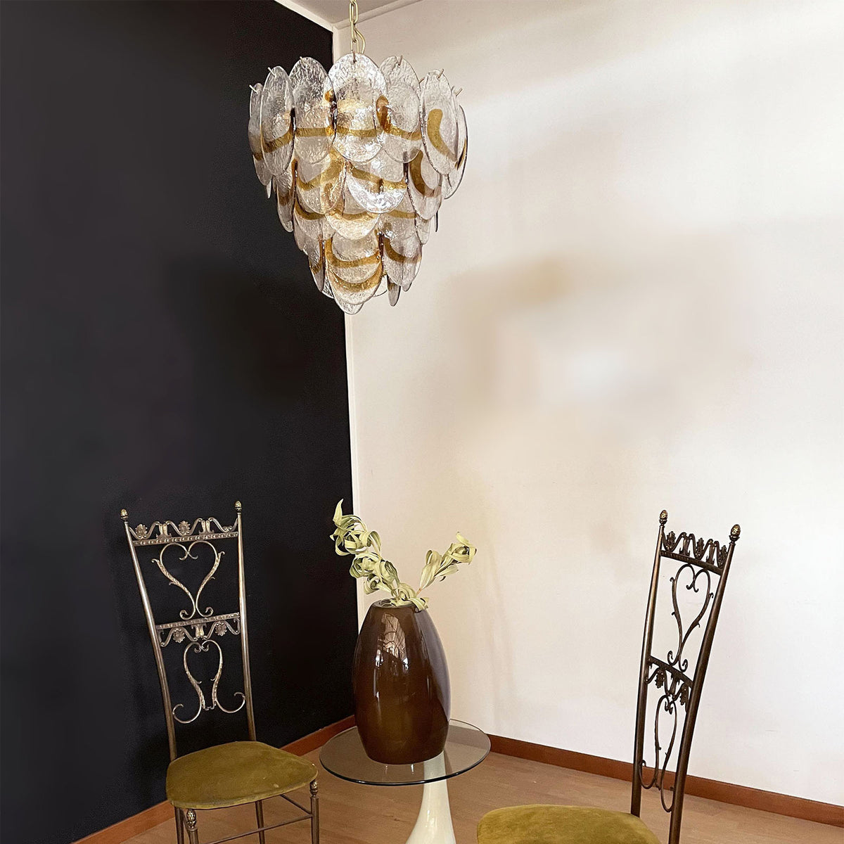 Lit Mazzega-style glass chandelier against a dark wall, casting a warm ambient glow.
