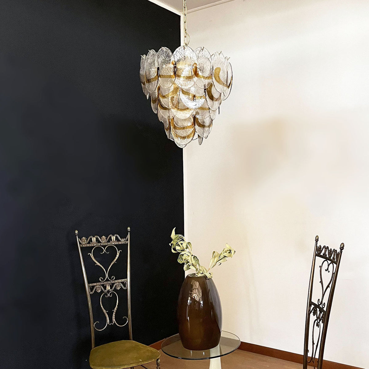 Mazzega-style glass chandelier hanging alone against a light-colored wall in a simple room.