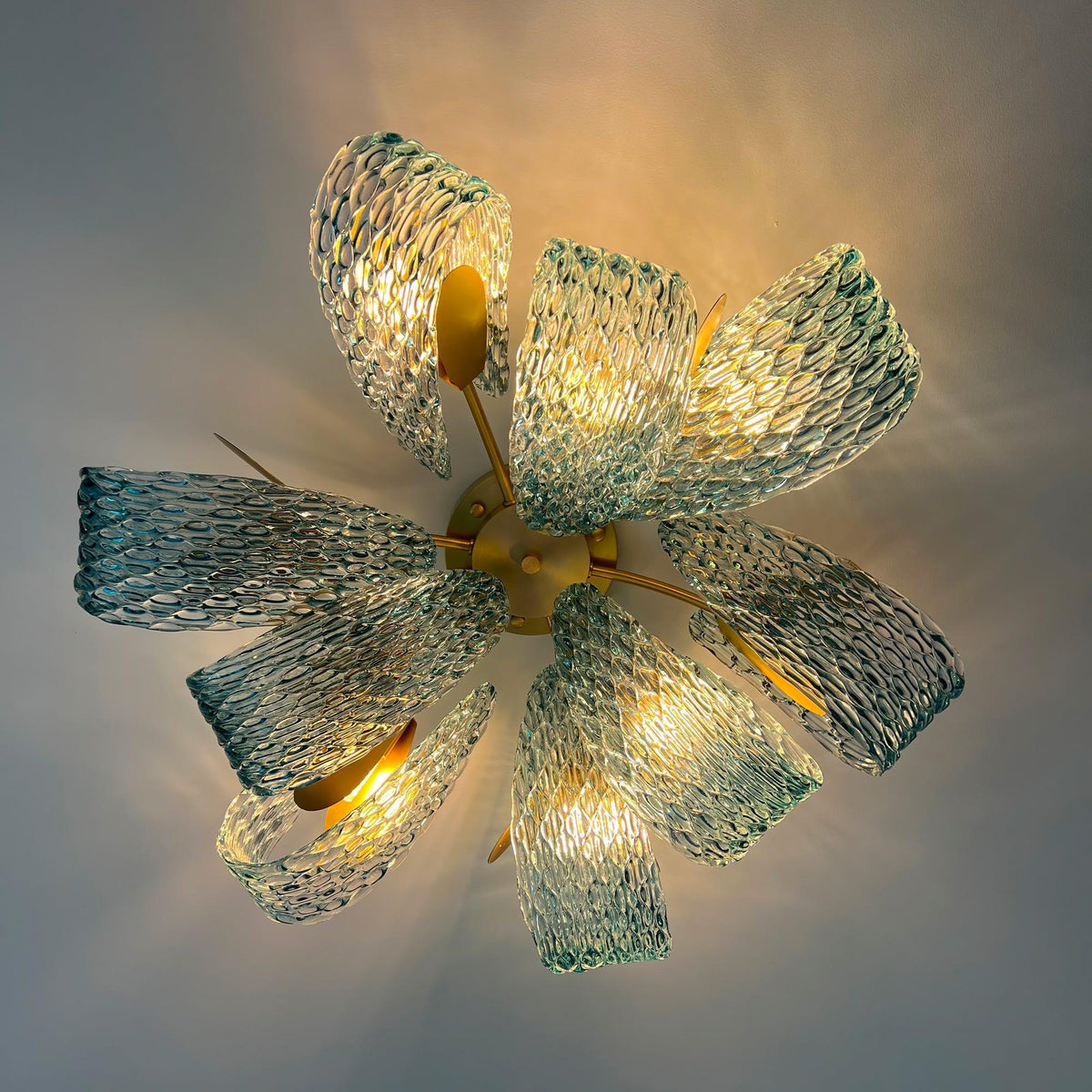 Lit petal blue glass ceiling light, showing warm light diffusing through the textured blue glass petals.