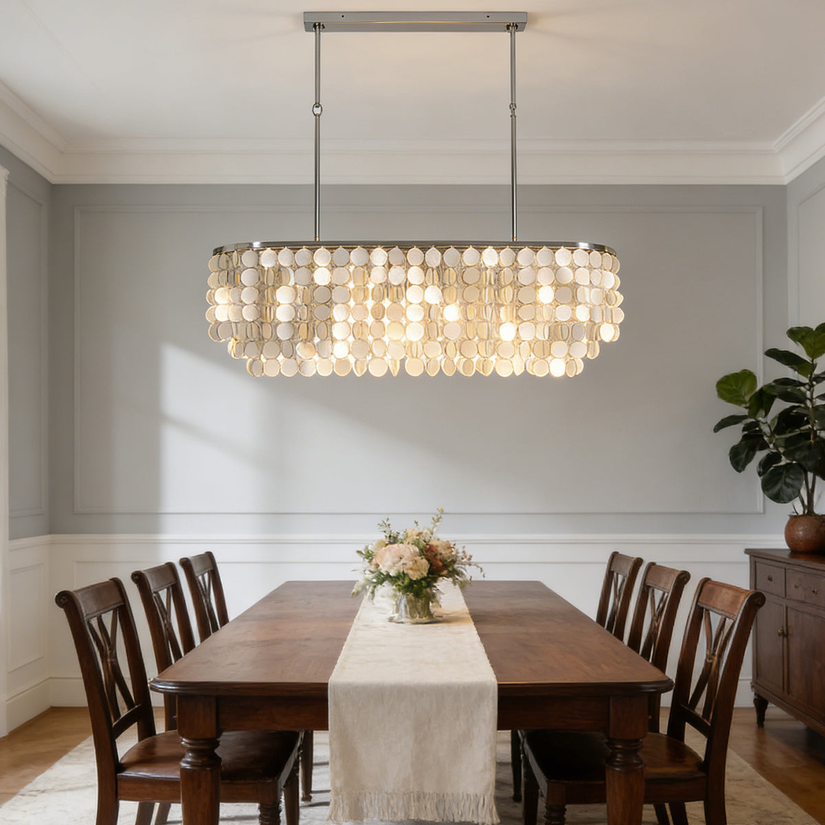 Rectangular capiz shell chandelier centered above a wooden dining table with upholstered chairs.