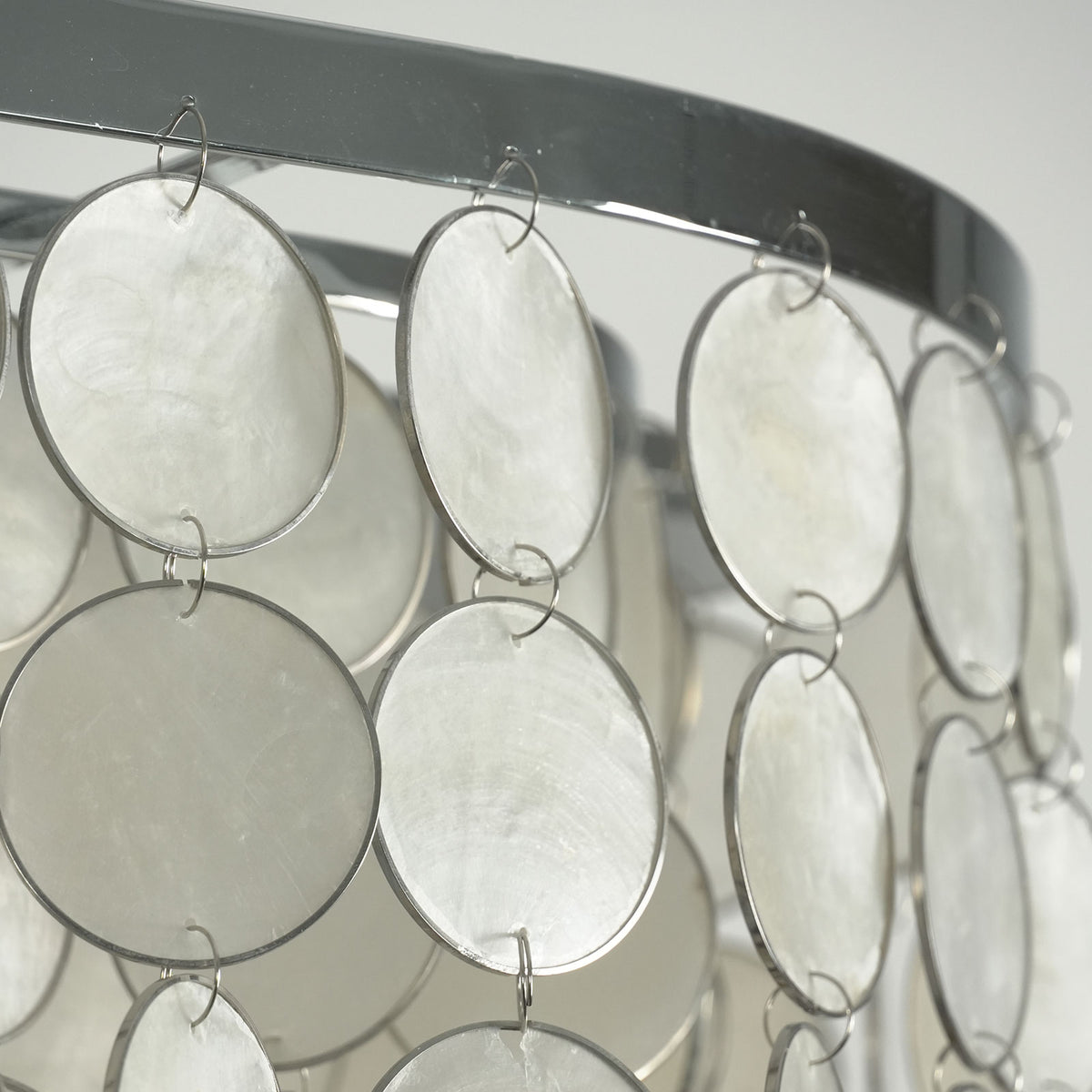 Close-up of the polished chrome frame and hanging capiz shell discs on the rectangular chandelier.