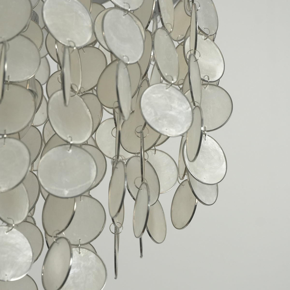 Close-up of the cascading capiz shell discs on the rectangular chandelier, showing their natural drape.