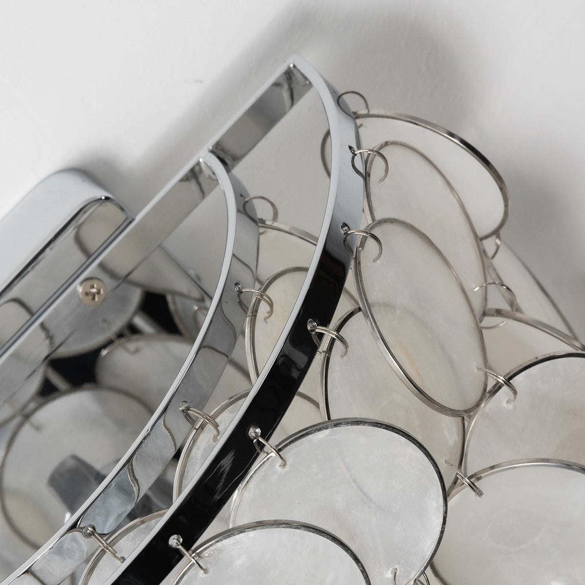 Close-up of the polished chrome frame and hanging hardware on the capiz shell wall sconce.