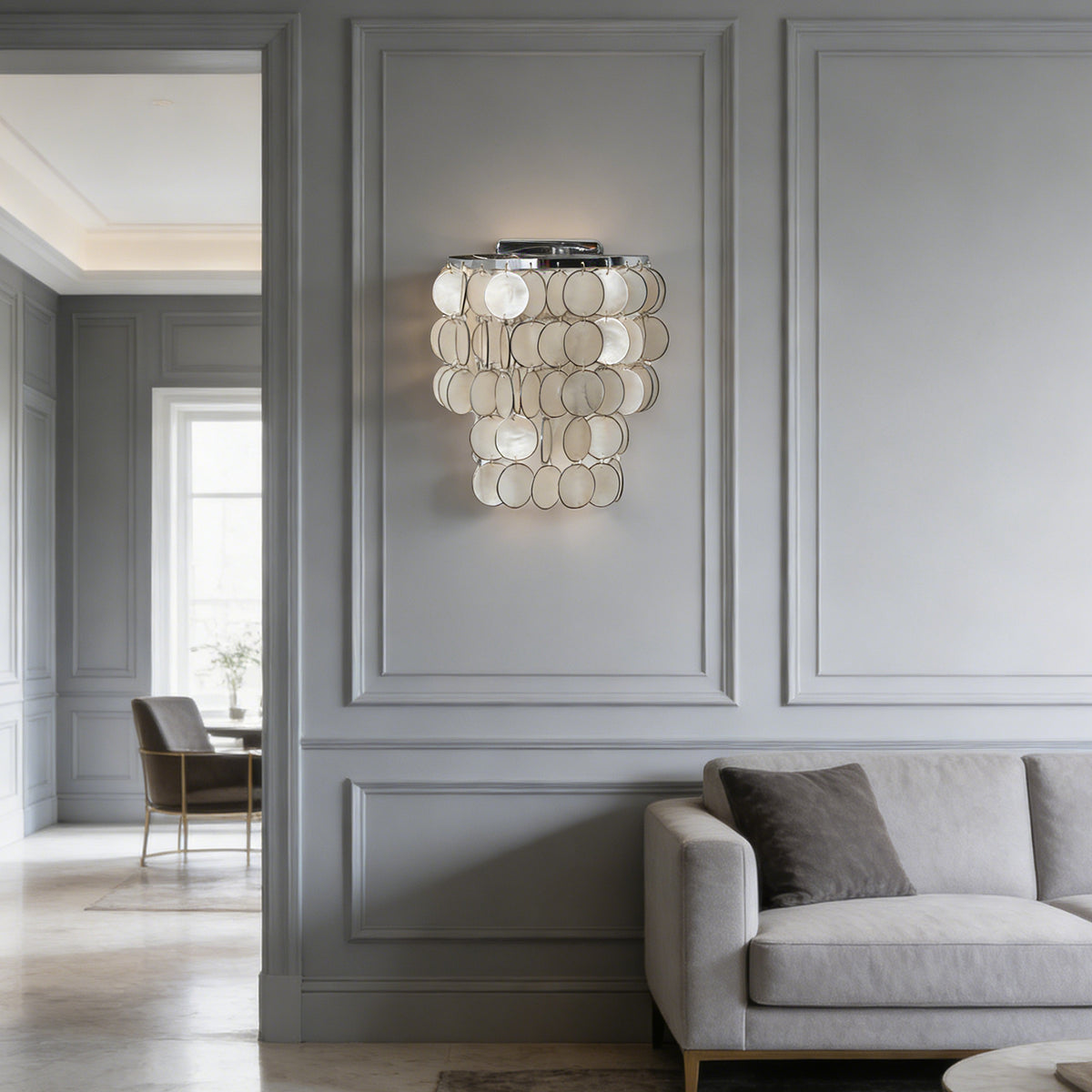 Round tiered capiz shell wall sconce mounted in a bright hallway with light gray paneled walls.