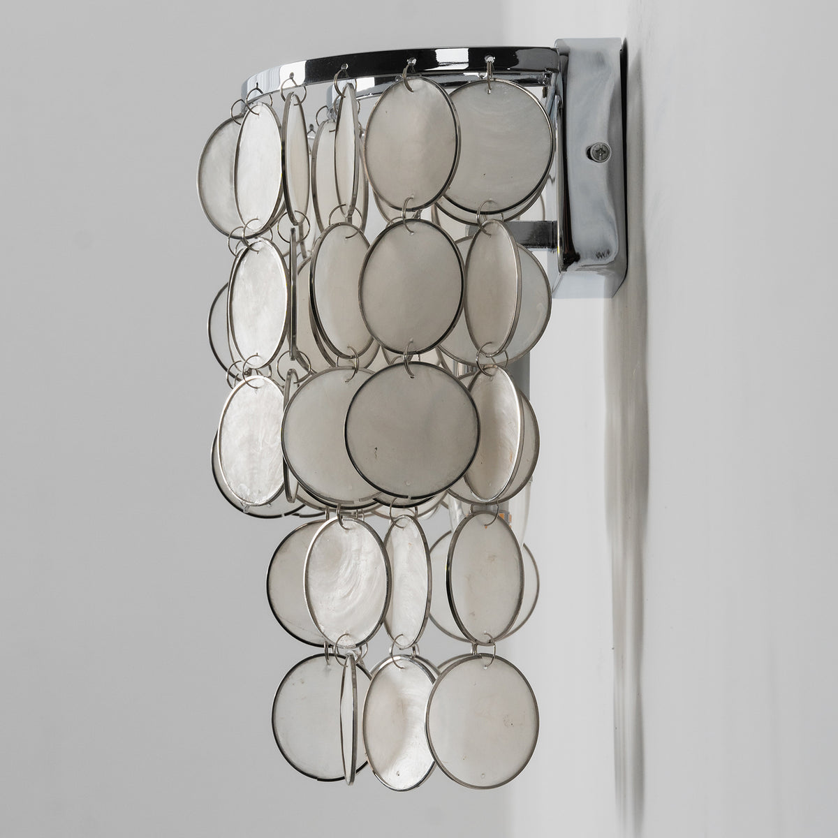 Side view of the installed round tiered capiz shell wall sconce, showing its wall mount and shell layers.