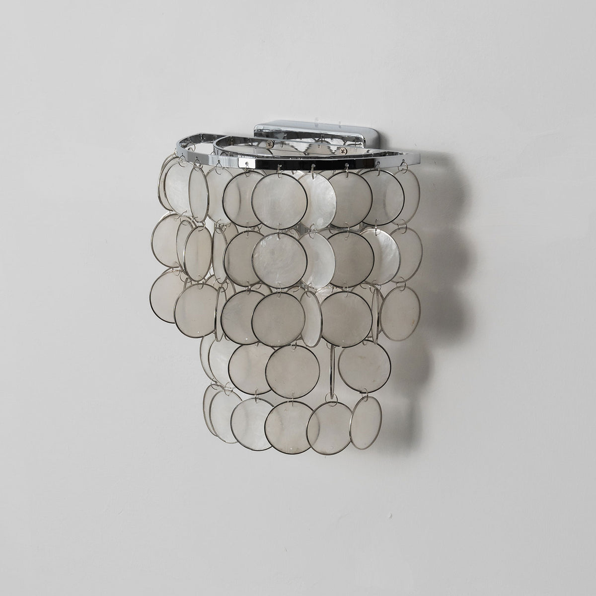 Lit round tiered capiz shell wall sconce highlighting the translucent texture of the capiz shells.