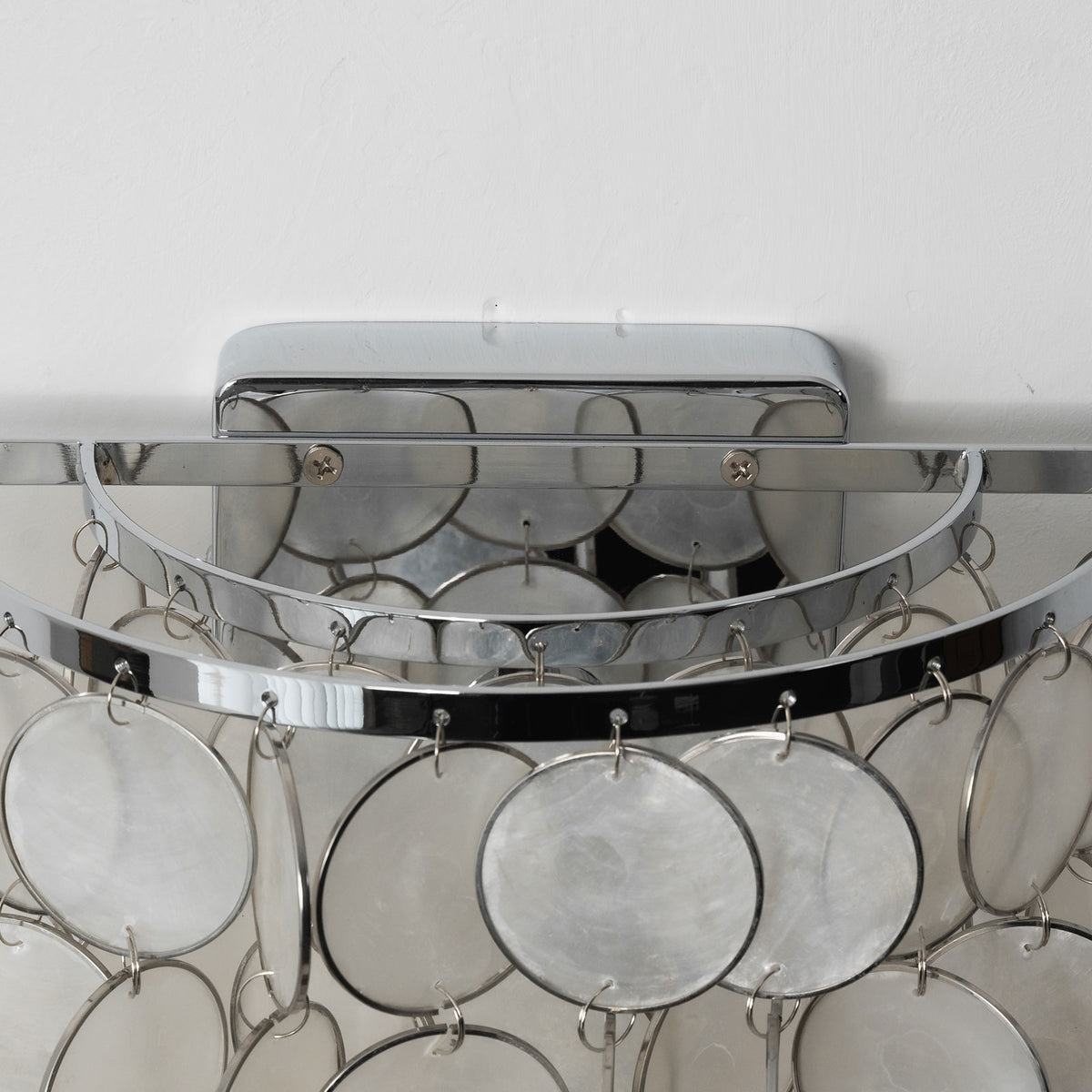Close-up of the metal wall mount and frame on the round tiered capiz shell wall sconce.