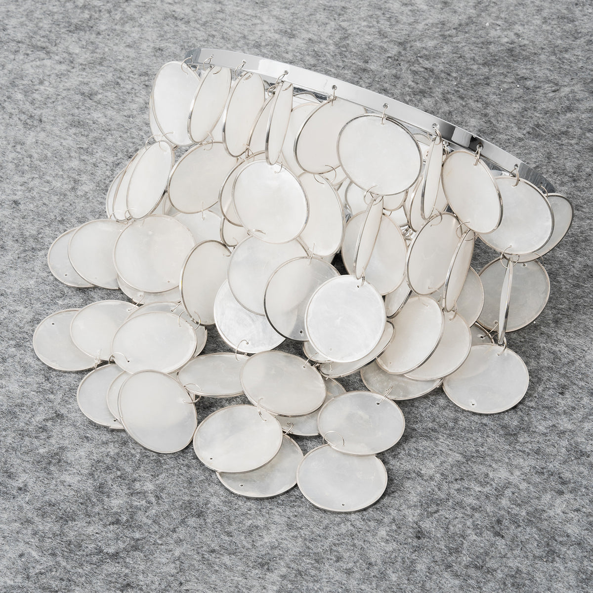 Loose capiz shell discs for the round tiered wall sconce, laid out on a gray textured surface.