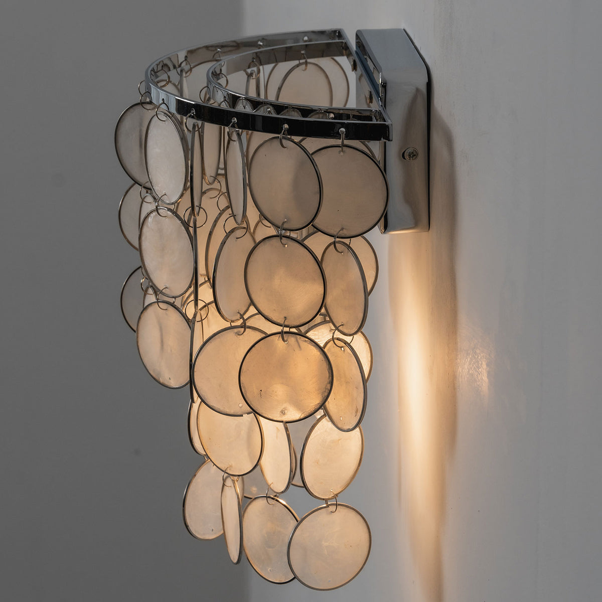 Side view of a lit round tiered capiz shell wall sconce, showing light glowing through the shells.