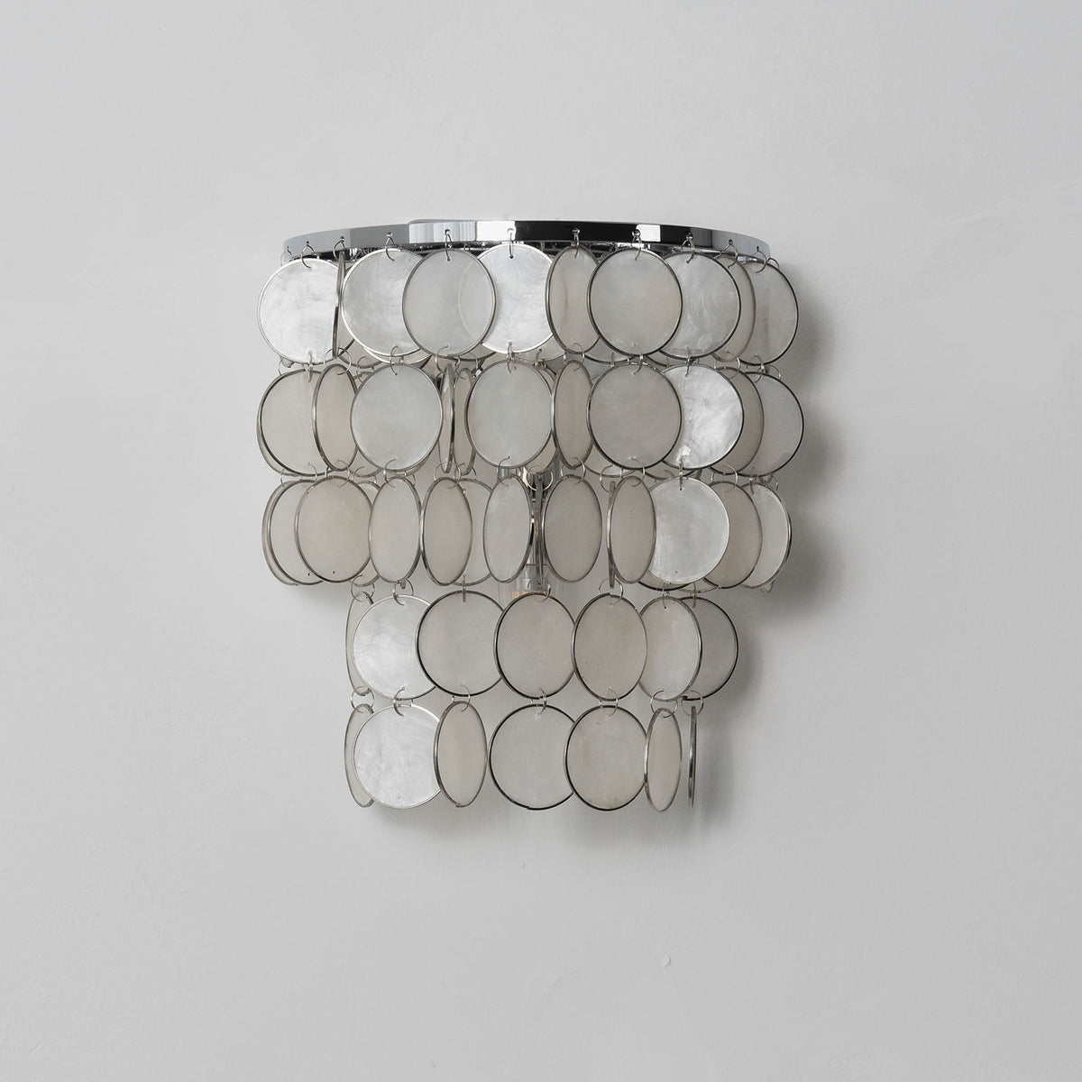Single round tiered capiz shell wall sconce against a light neutral background.