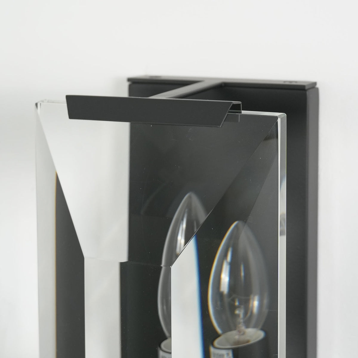 Lit single-headed crystal wall lamp with black frame, casting soft light through crystal panels.