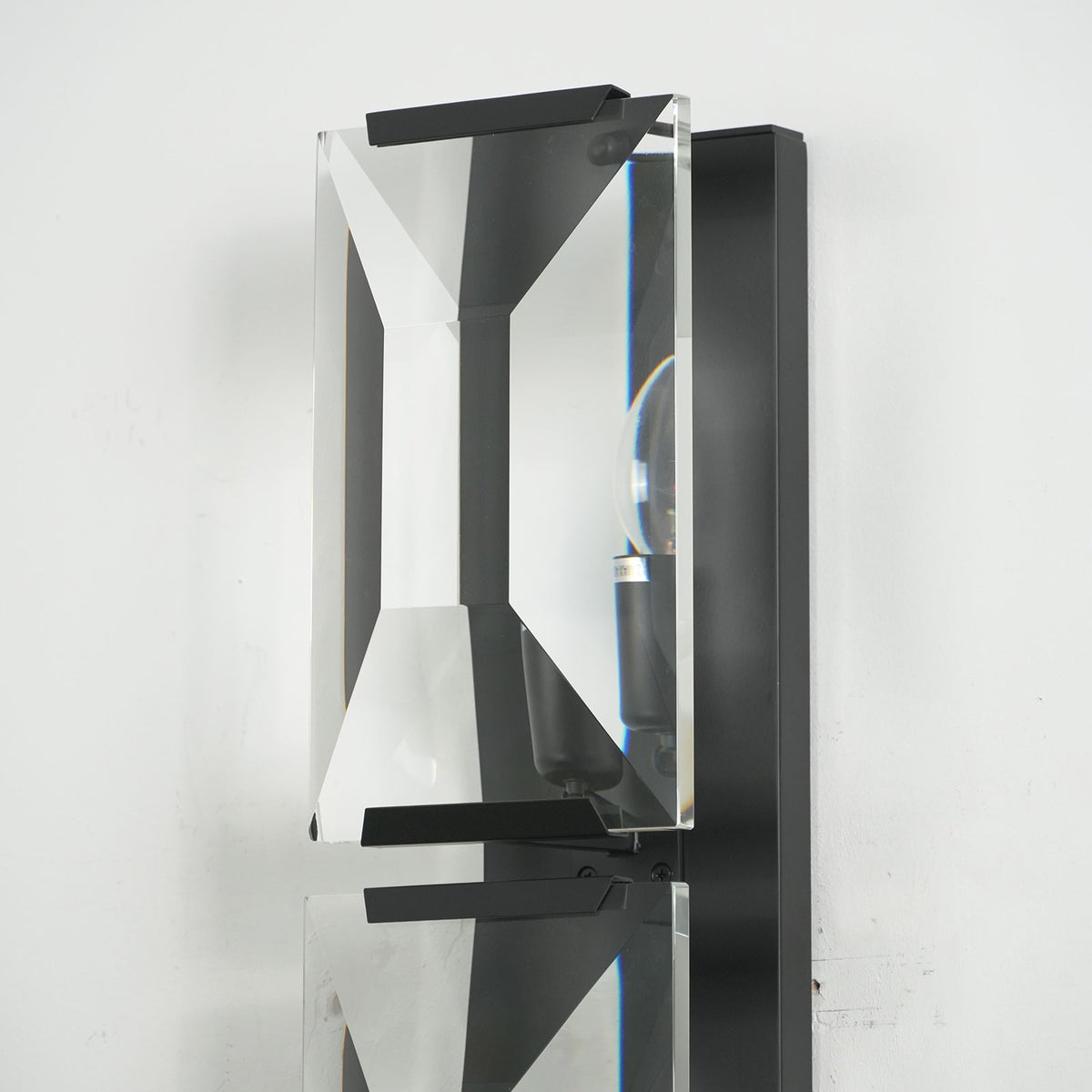 Lit three-headed crystal wall lamp with black frame, showing its crystal facets and warm glow.