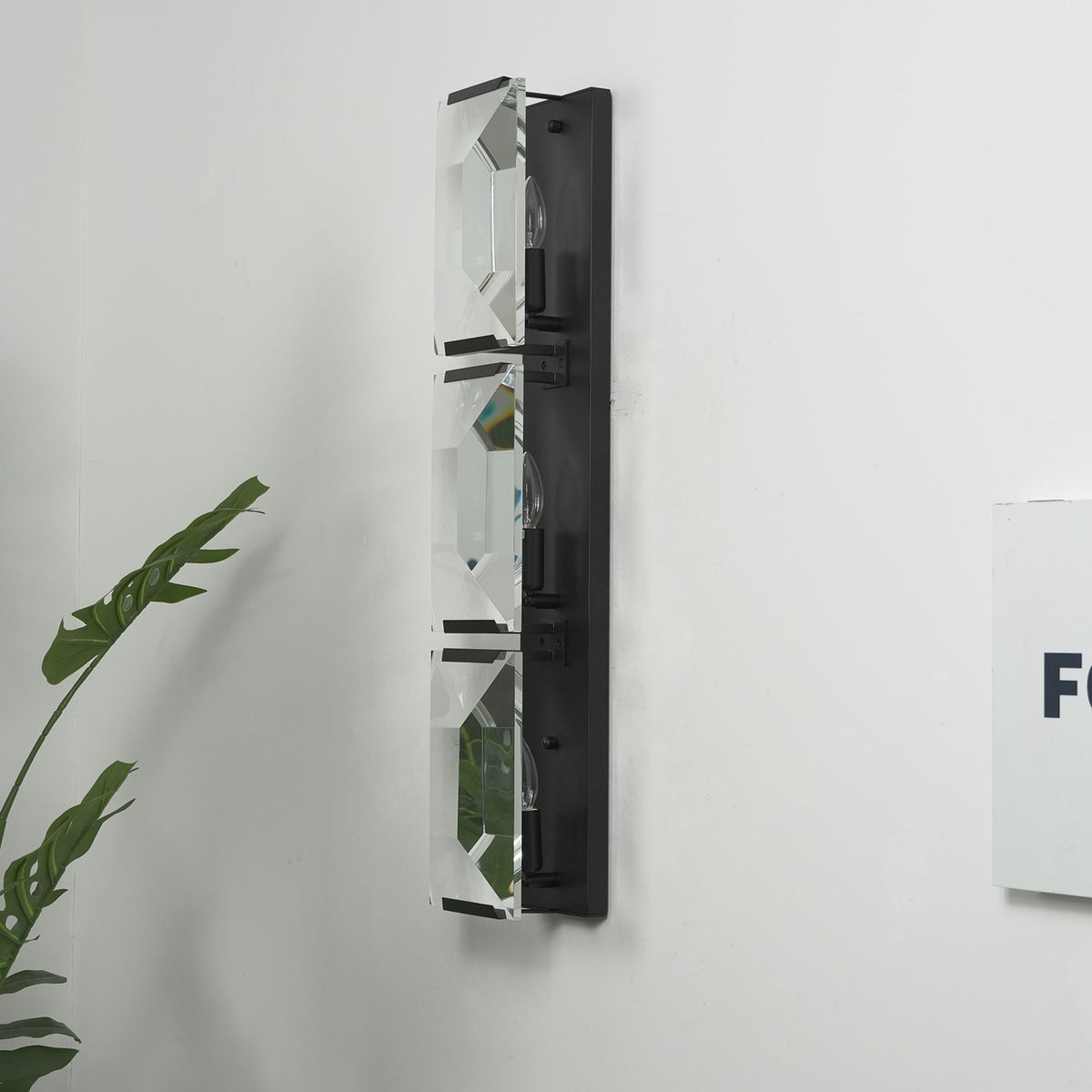 Side view of the three-headed crystal wall lamp with black frame, isolated on a white background.