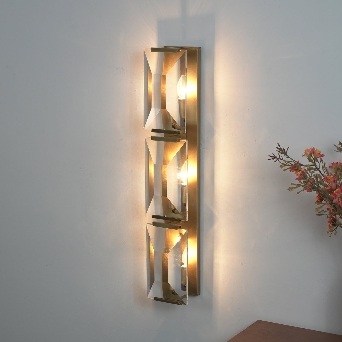 Lit three-headed crystal wall lamp, showing light reflecting off faceted crystal panels.