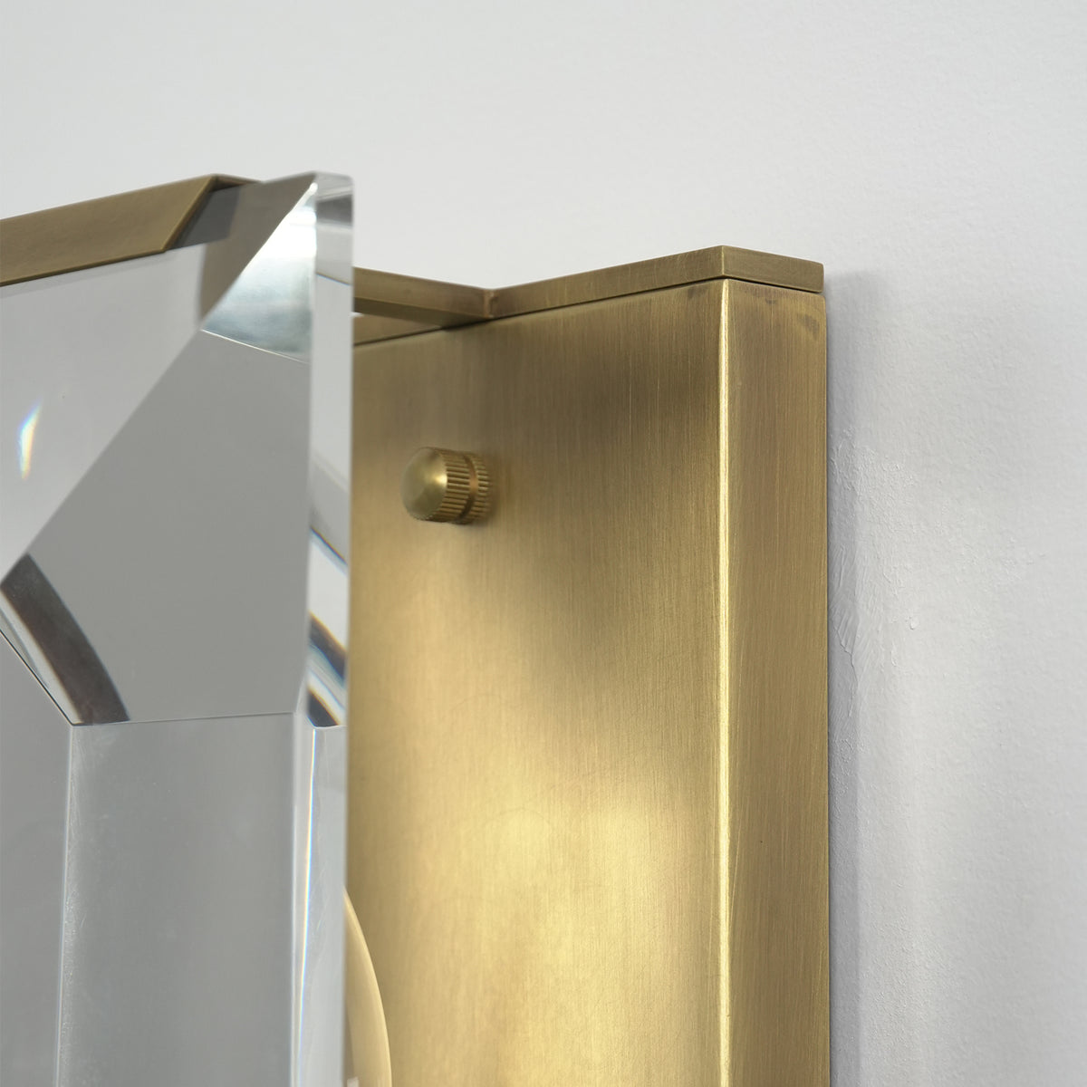 Side view of a lit three-headed crystal wall lamp, highlighting its brass frame and crystal facets.