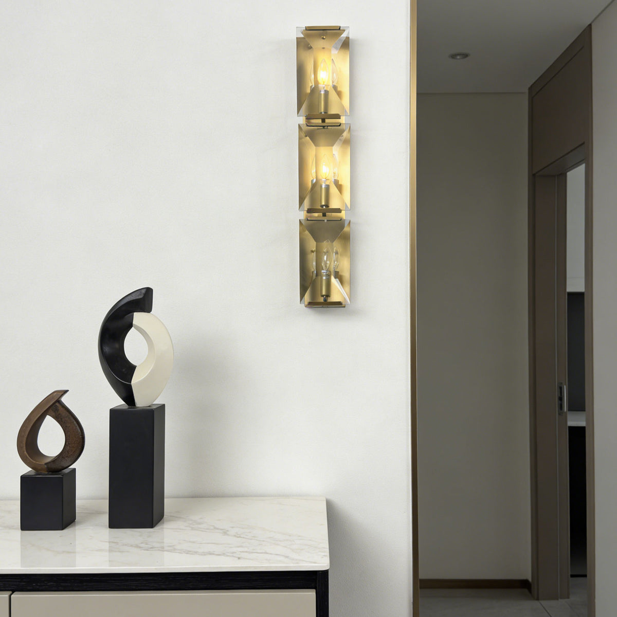 Three-headed crystal wall lamp in a minimalist entryway with modern decor.