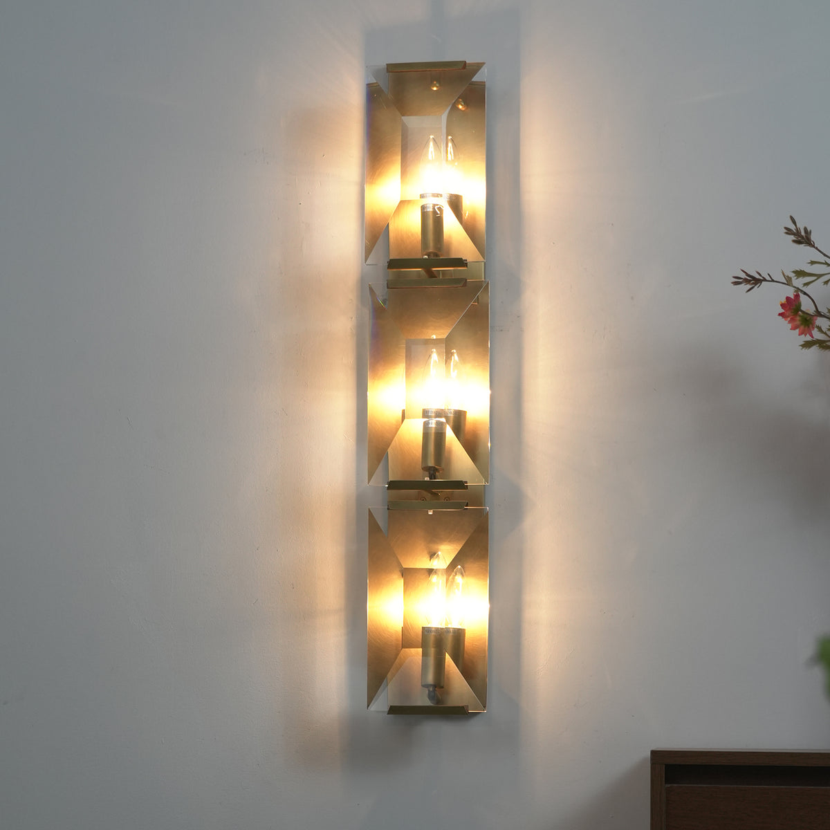 Lit three-headed crystal wall lamp on a warm neutral wall, casting soft light through faceted crystals.
