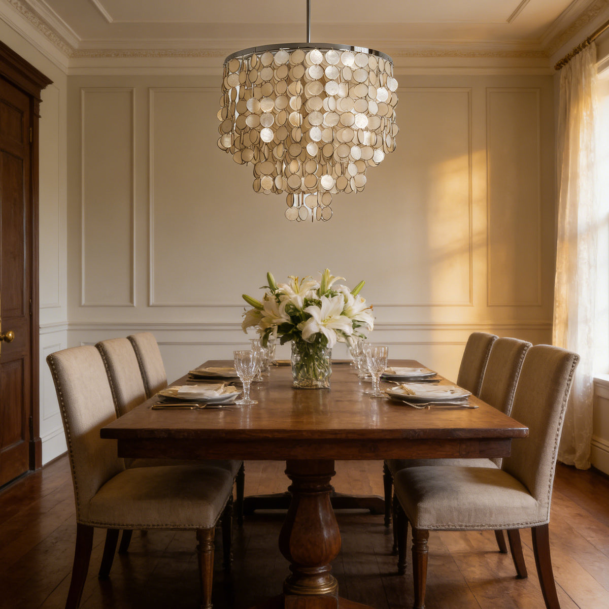 Tiered capiz shell chandelier centered above a wooden dining table with upholstered chairs.