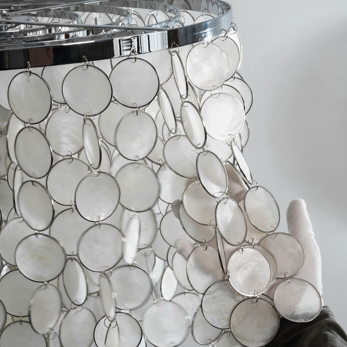 Close-up of the polished chrome frame and hanging hardware on the tiered capiz shell chandelier.