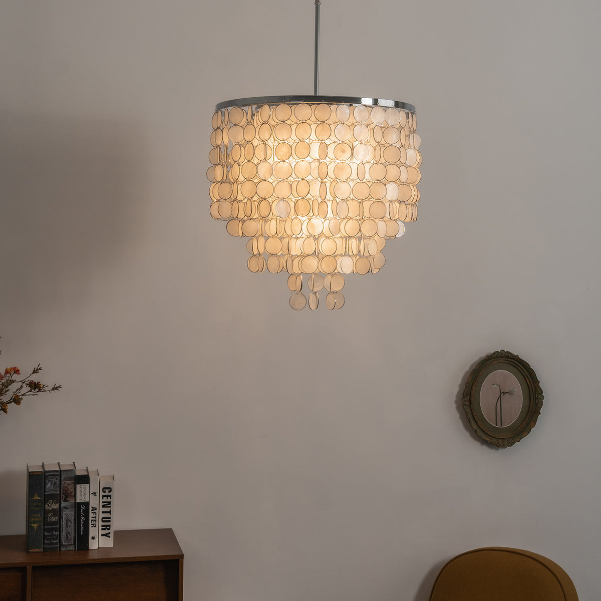 Tiered capiz shell chandelier hanging alone against a light-colored wall, showing its full shape.