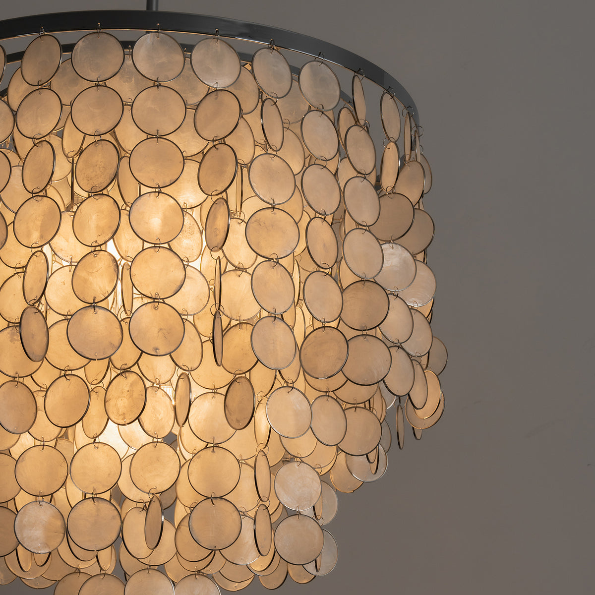 Close-up of a lit tiered capiz shell chandelier, showing how light filters through natural shell discs.