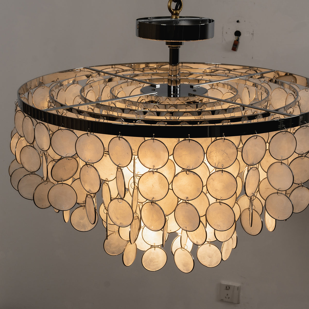 Tiered shell disc ceiling light with a black ceiling mount, lit with warm ambient light.