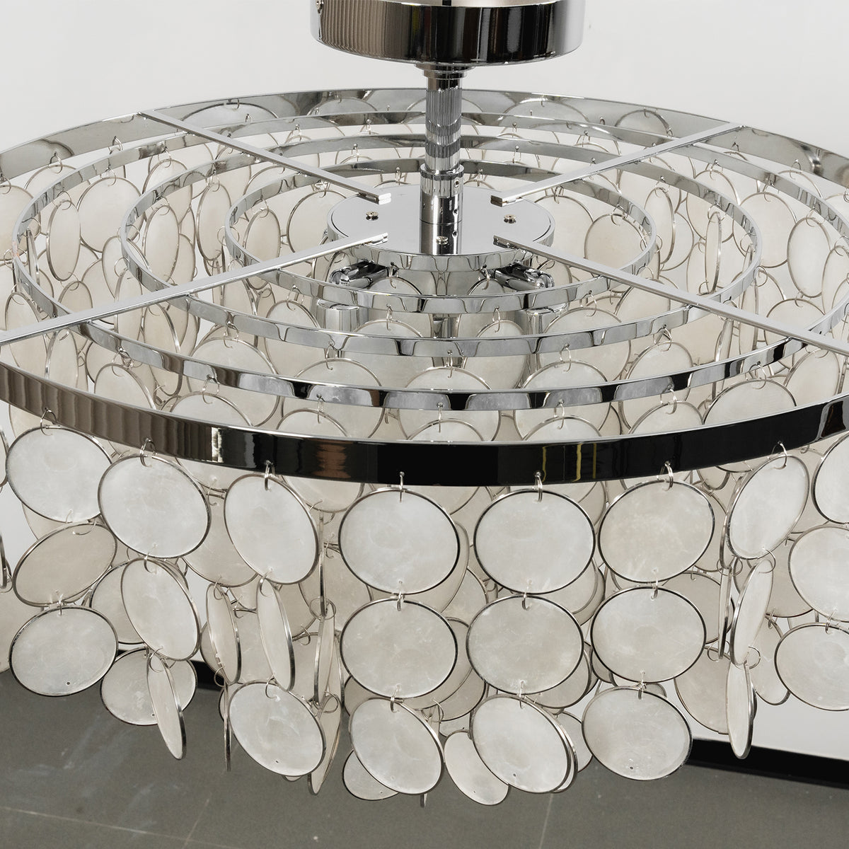 Close-up of the metal ceiling mount and tiered shell disc structure of the ceiling light.
