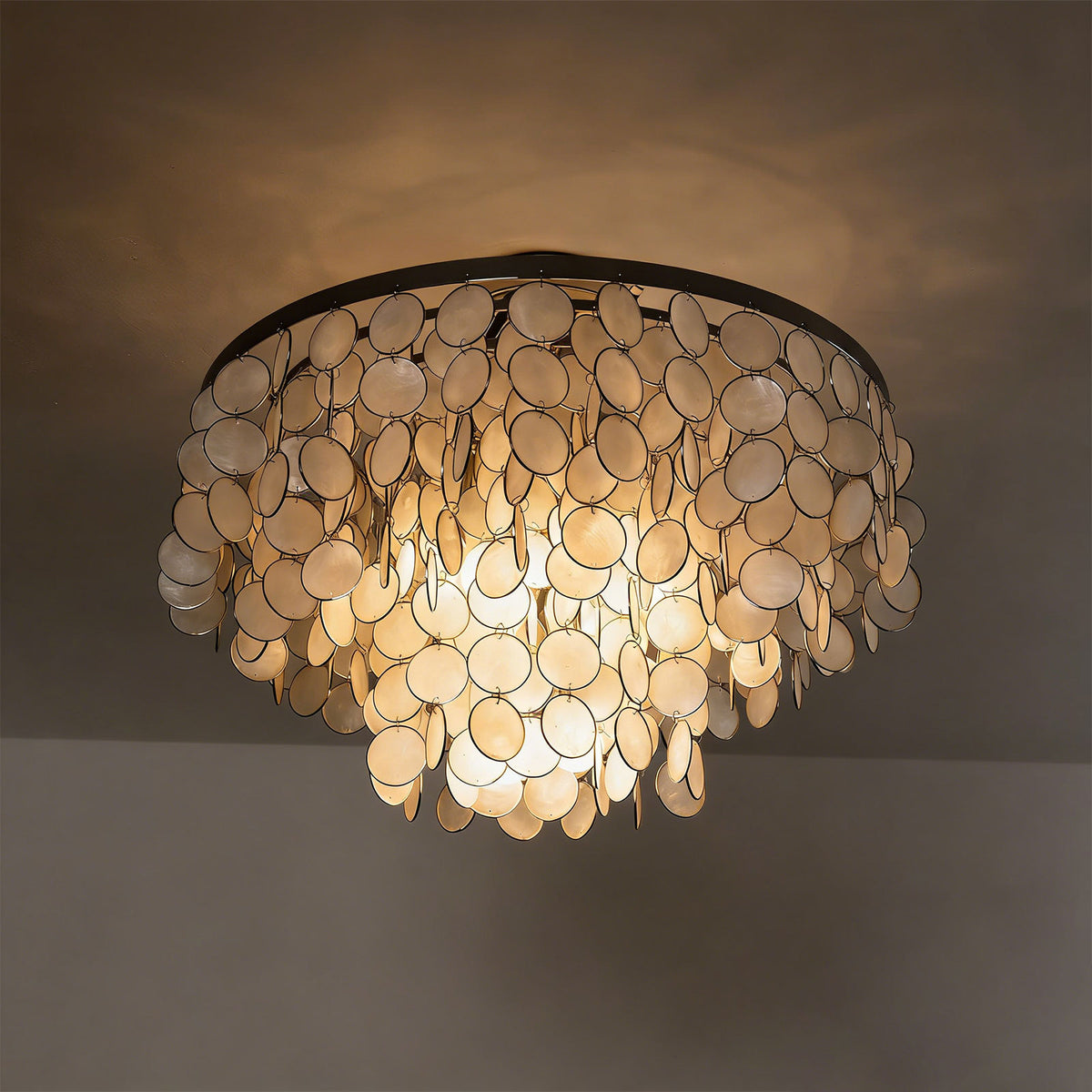 Close-up of a lit tiered shell disc ceiling light, showing how light filters through the natural shells.