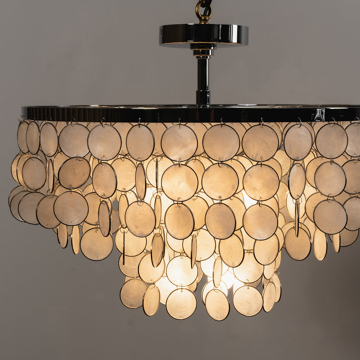 Lit tiered shell disc ceiling light casting a warm golden glow against a dark background.