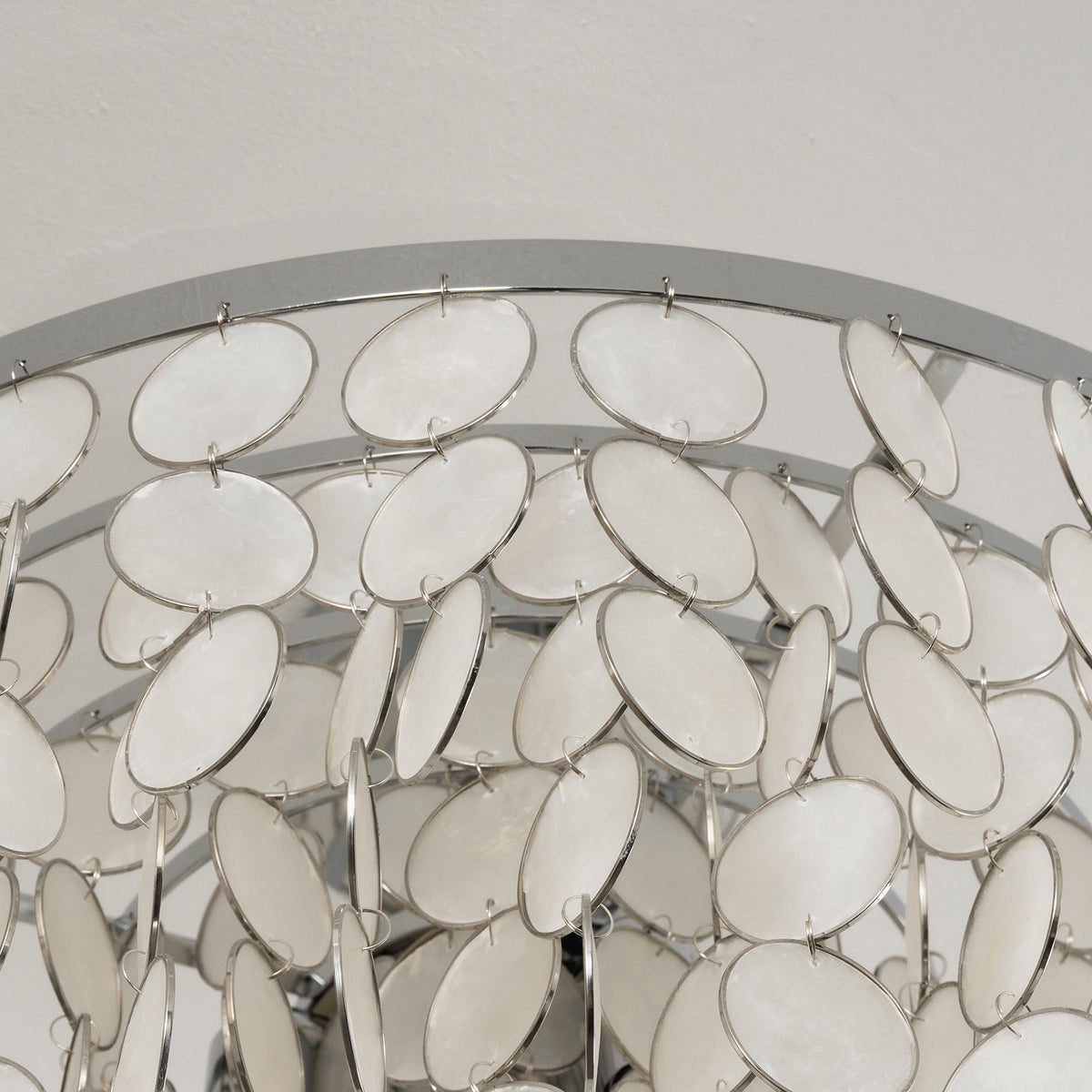 Close-up of the polished metal rim and hanging capiz shell discs on the tiered ceiling light.