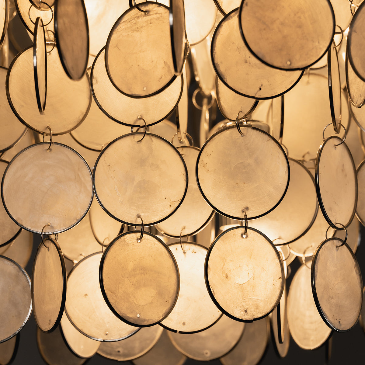 Close-up view of glowing capiz shell discs on the tiered ceiling light, highlighting their translucent texture.